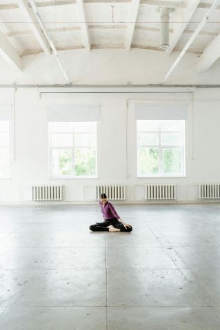 A dancer performs a pose in a spacious, sunlit ballet studio.